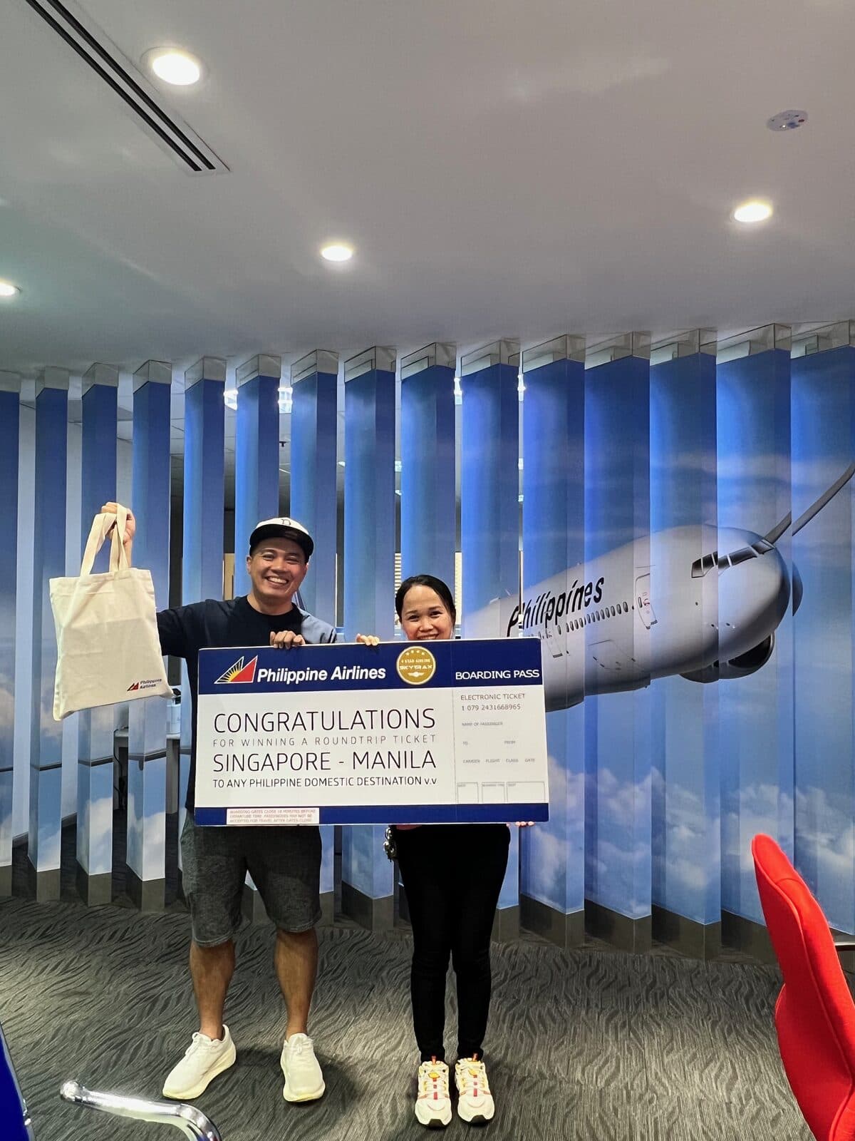 FIS Editorial and the Christmas Wishing Tree winner at the Philippine Airlines Singapore office, holding a Singapore–Manila roundtrip boarding-pass display