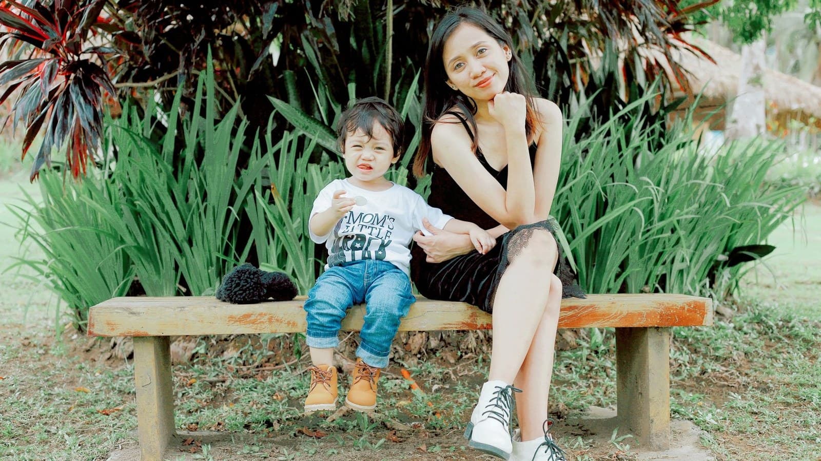 A smiling Filipina mother and her young son sitting on a park bench