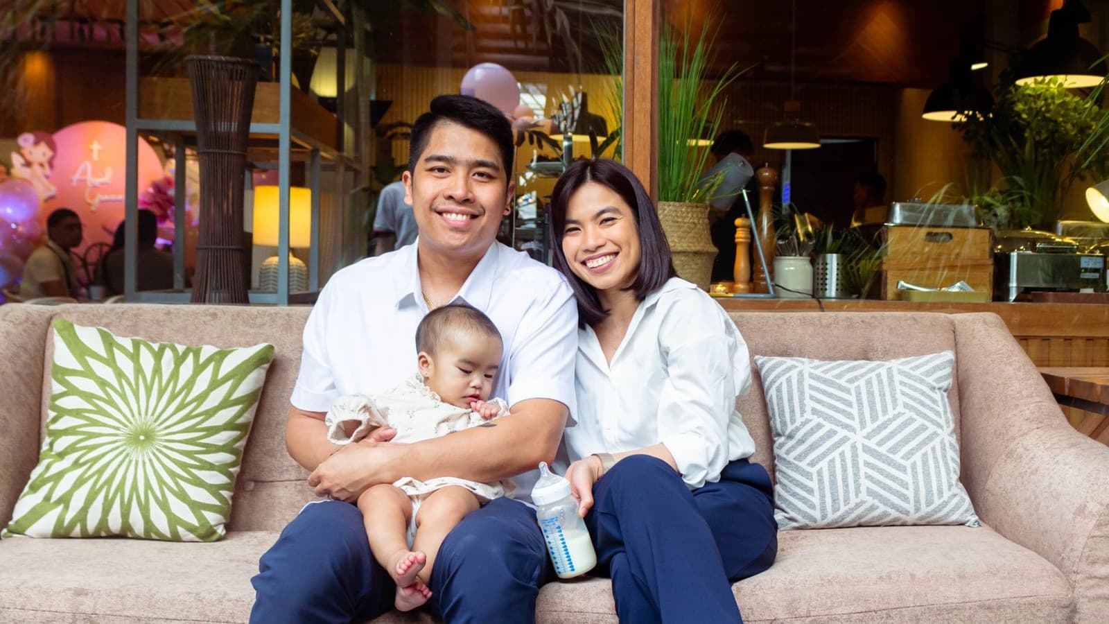 A smiling Filipino couple with their baby on a sofa