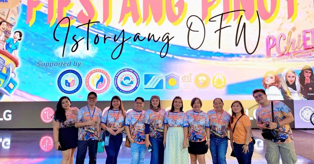The Fiestang Pinoy 2026 committee in matching festival shirts stand in front of the LED stage backdrop reading Fiestang Pinoy: Istoryang OFW, with the supporting partners' logos including the Philippine Embassy, Migrant Workers Office Singapore, OWWA, SSS, HOME and DTI