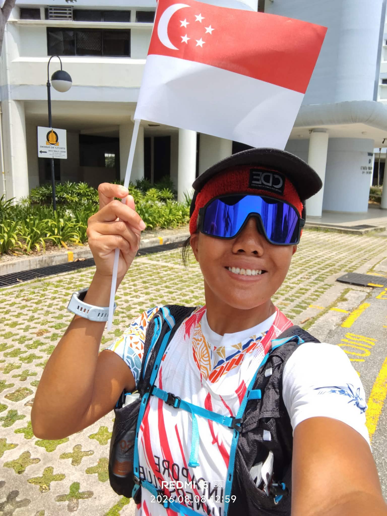 Jeanette Camilo Cariso smiling in running gear and cap, holding a small Singapore flag after her 61km SG61 run
