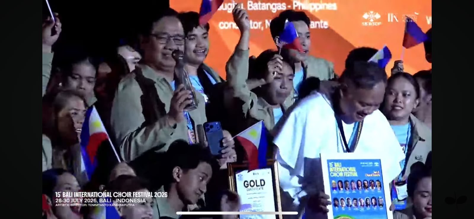 A gold certificate held up on stage at the 15th Bali International Choir Festival